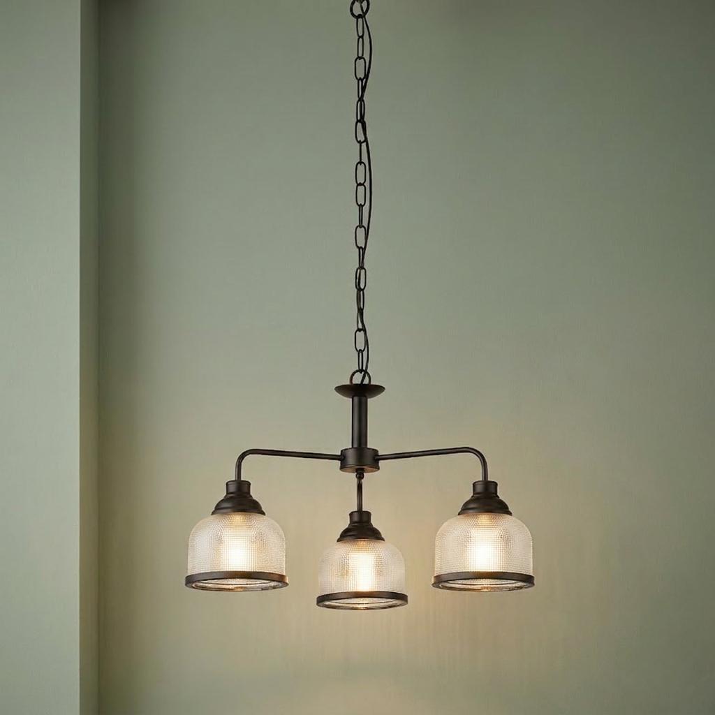 Three-light black pendant with holophane style glass shades hanging against a light green wall.