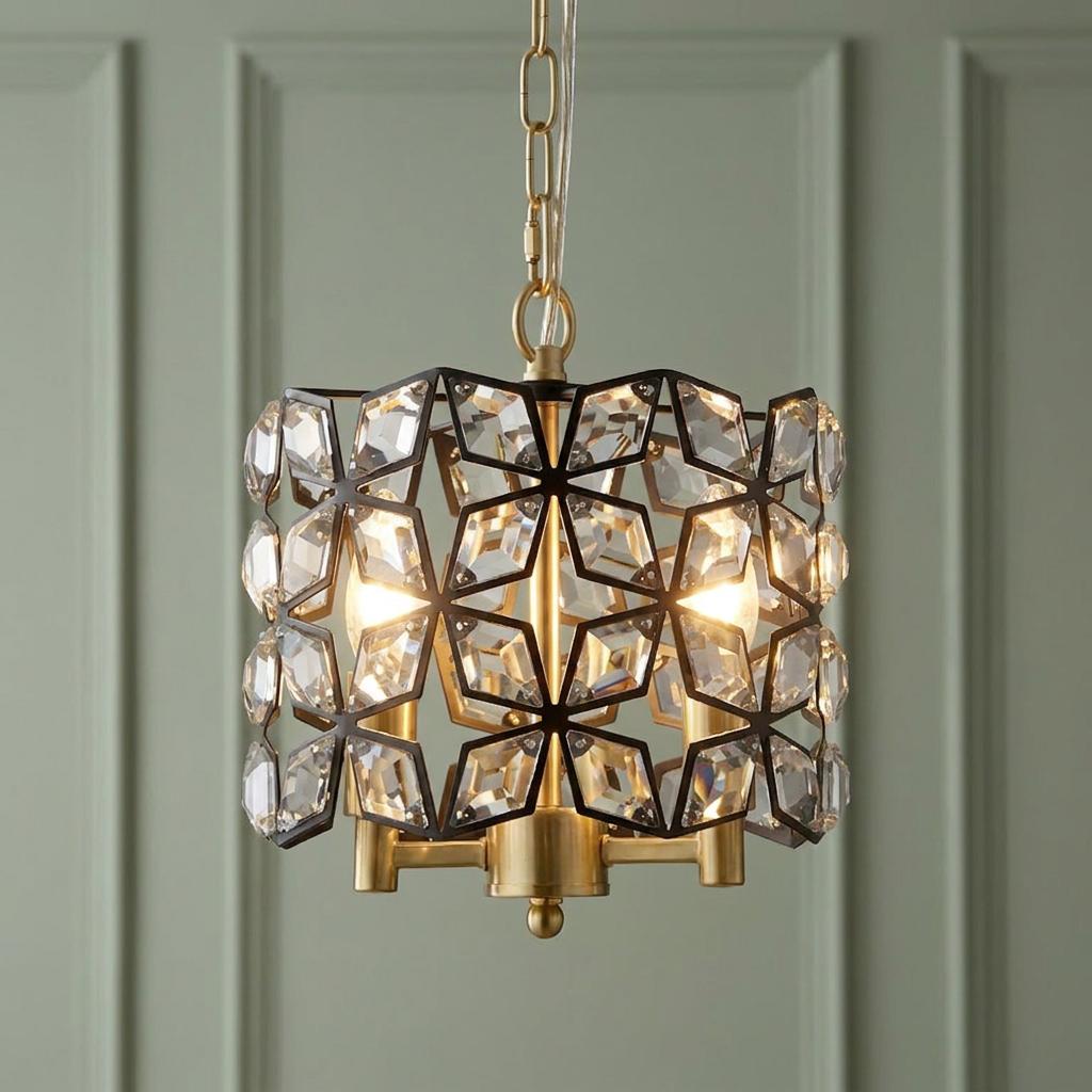 A black geometric pendant light with crystal inserts and brass accents, glowing against a green paneled wall.