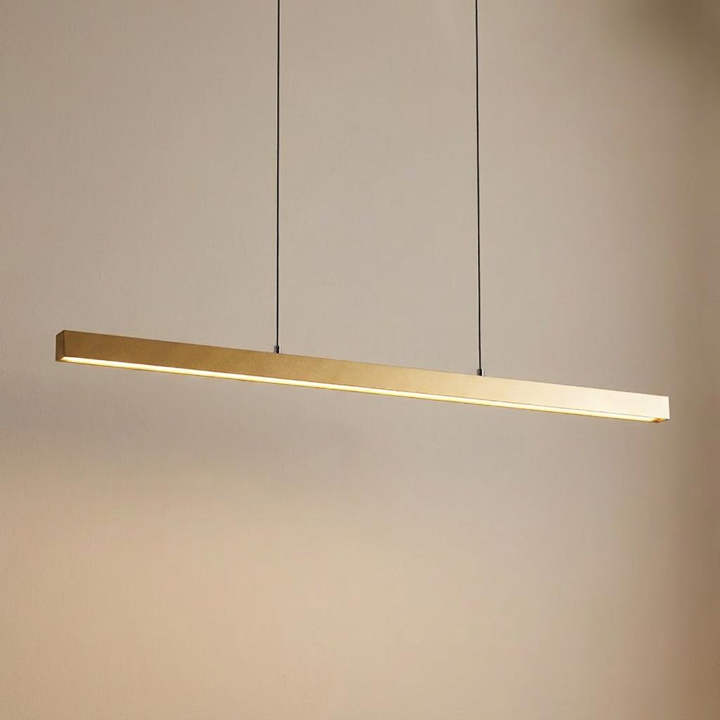 Gold LED bar pendant light with warm illumination hanging from two thin cables against a neutral wall.