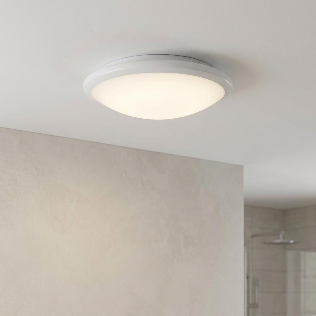 Circular white flush ceiling light with frosted glass illuminated in a minimalist bathroom.