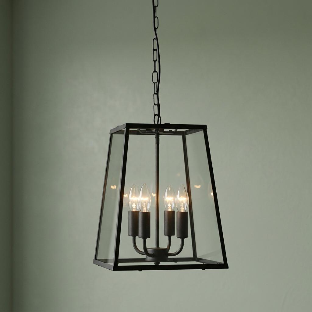 A black four-light lantern pendant with clear glass panels hanging against a pale green wall.