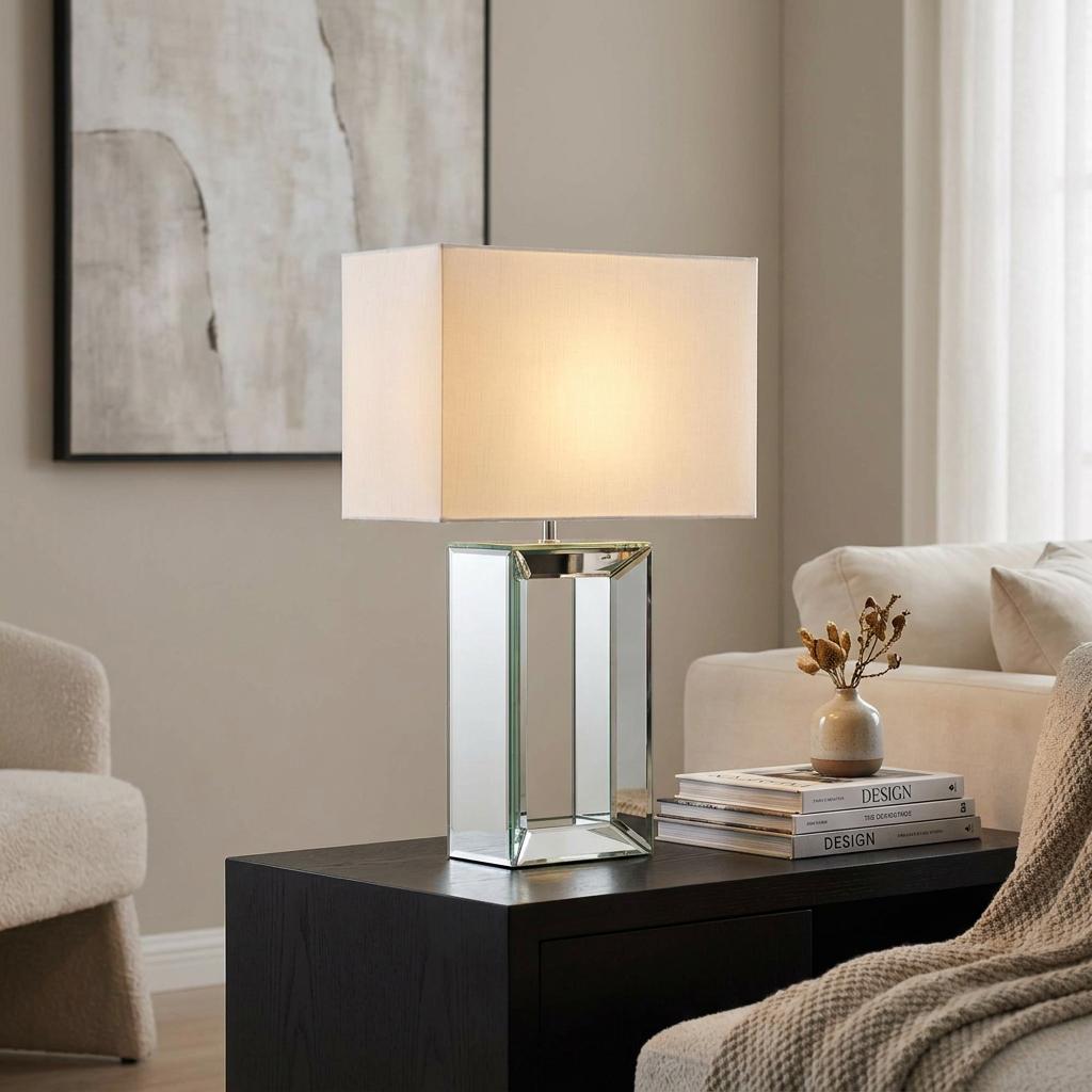 Rectangular mirrored table lamp with a white fabric shade on a black side table in a modern living room.