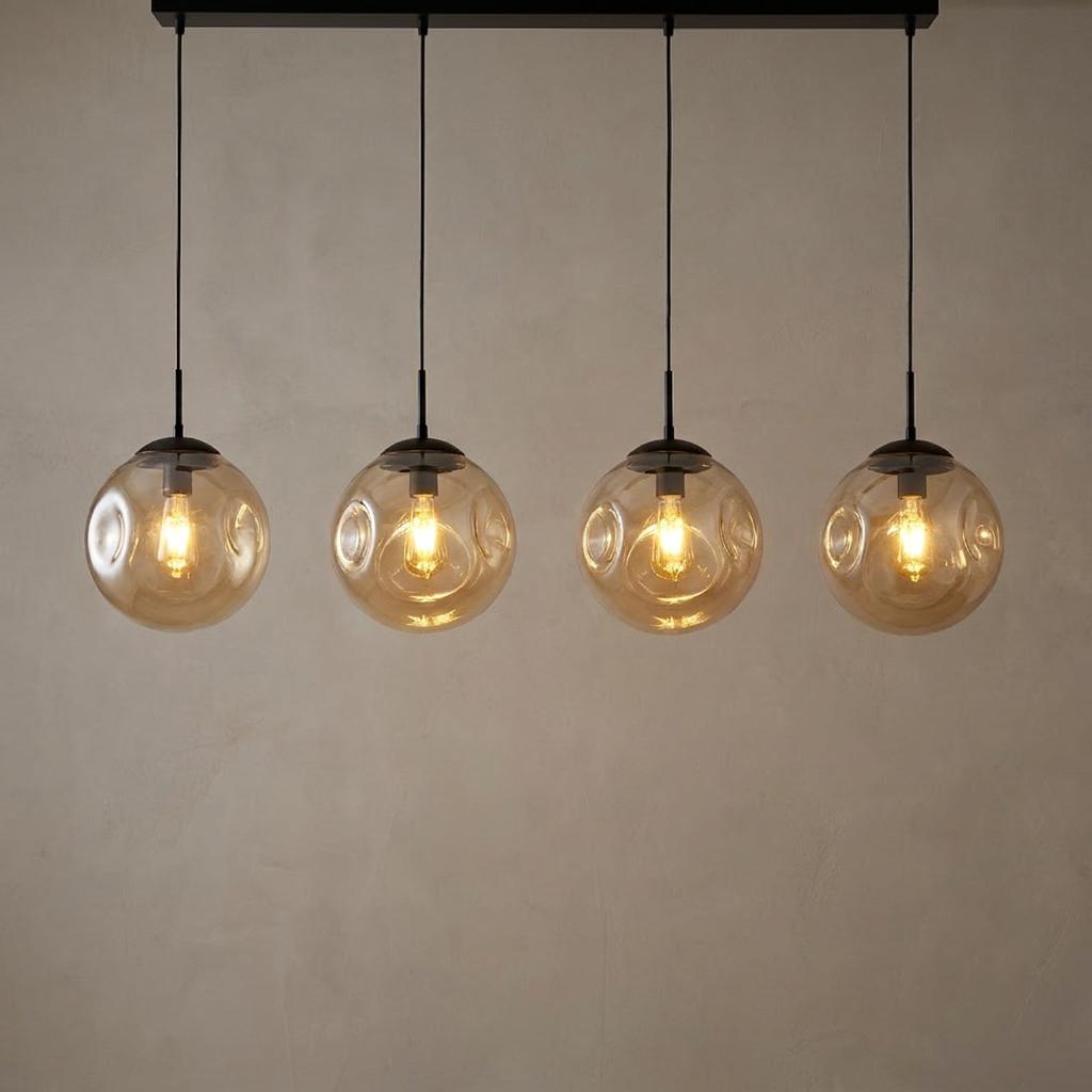 Four champagne punched glass globes hanging from a black bar, illuminated with warm bulbs against a neutral wall.