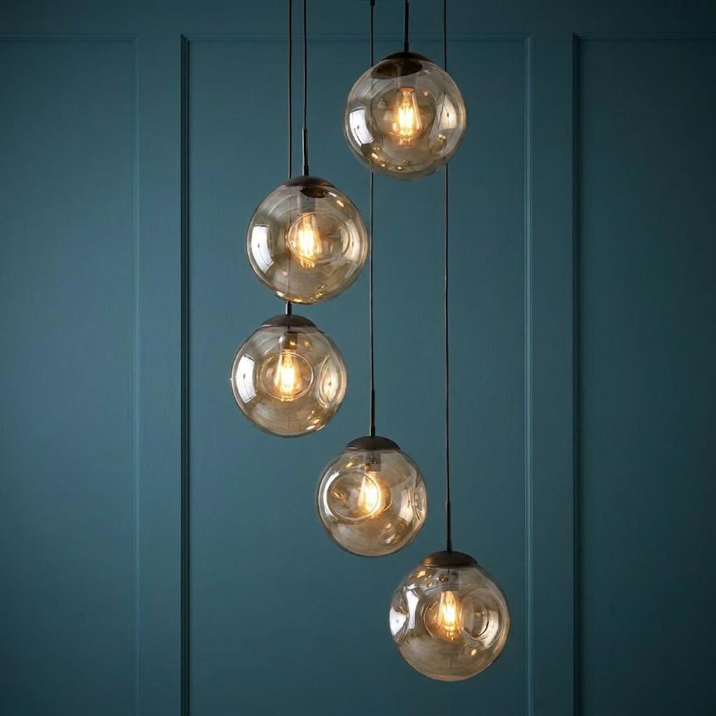 Five champagne glass globe pendant lights hanging at staggered heights against a teal paneled wall.