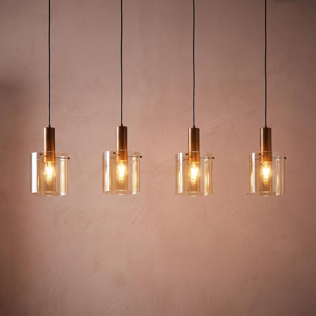 Four brown bar pendant lights with amber glass shades glowing against a textured wall.