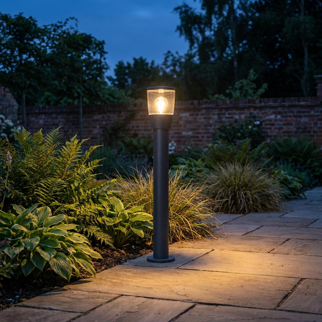 Warmly lit black bollard light beside a stone path in a garden at dusk.
