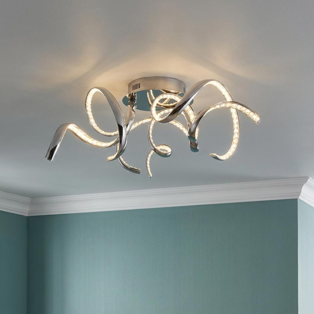 Modern chrome ceiling light with glowing swirling LED arms mounted on a white ceiling above teal walls.