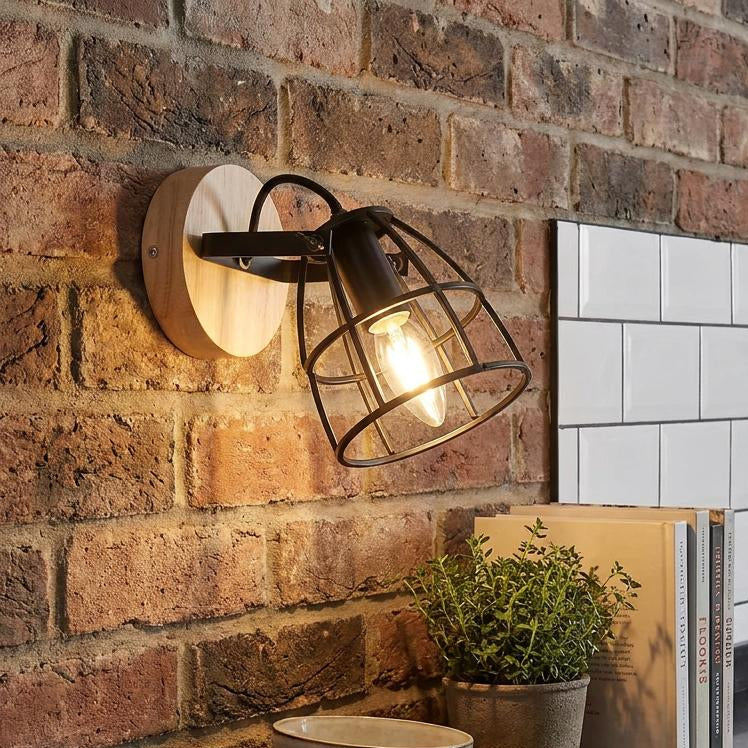 Industrial black cage wall light with a light wood base mounted on a rustic brick wall in a kitchen.