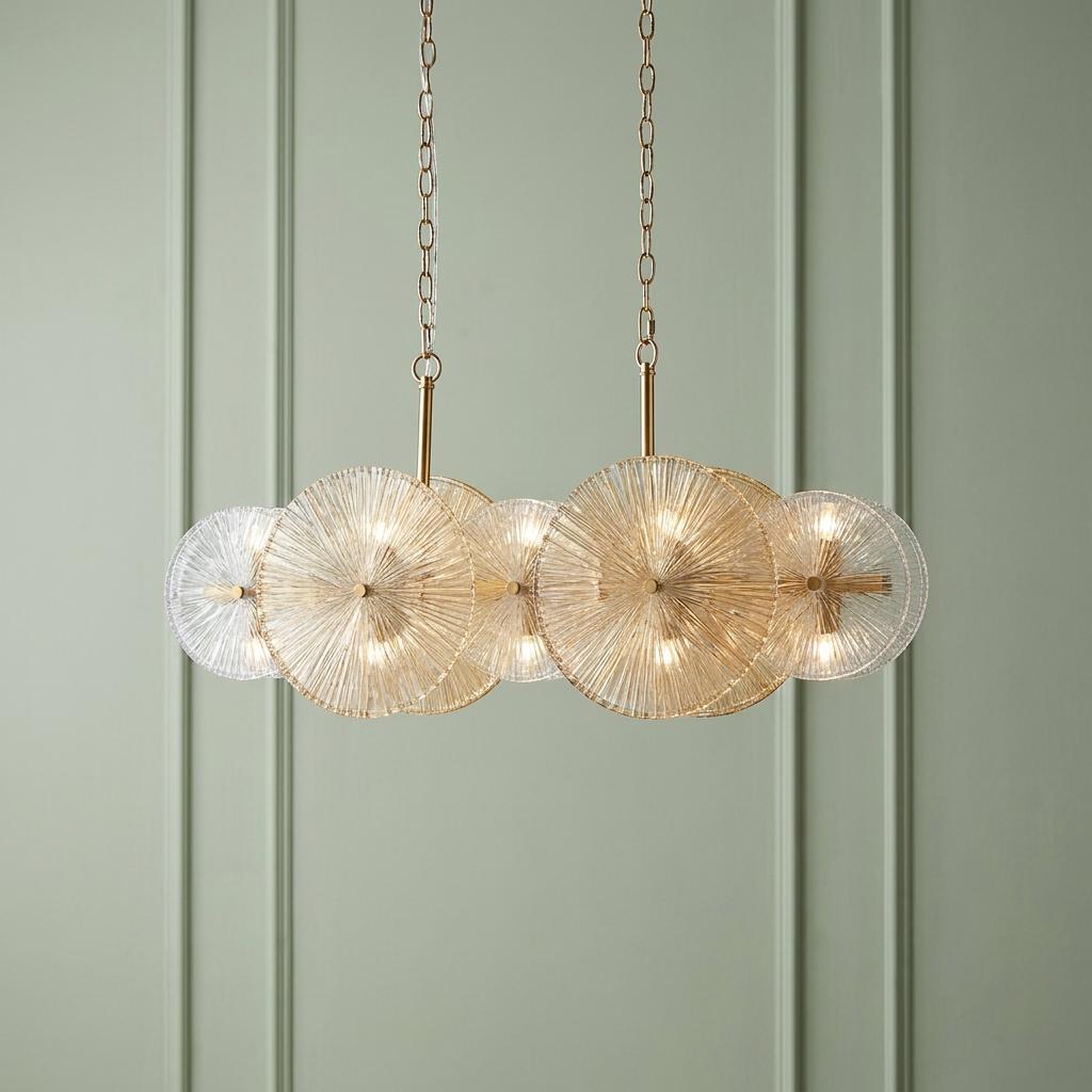 Bronze bar pendant light with sunburst ribbed glass discs hanging against a green paneled wall.