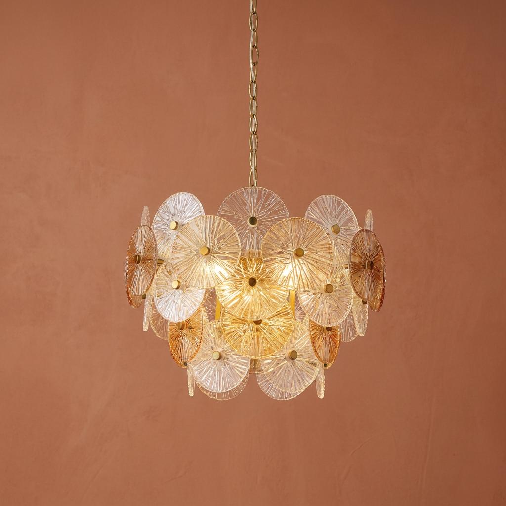 Modern tiered chandelier with clear and amber textured glass discs against a terracotta wall.