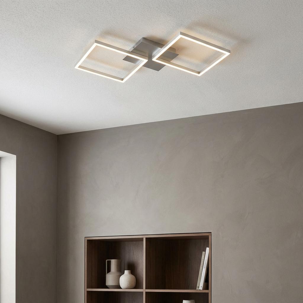 Modern silver ceiling light with two glowing LED square frames mounted in a minimalist room with gray walls.