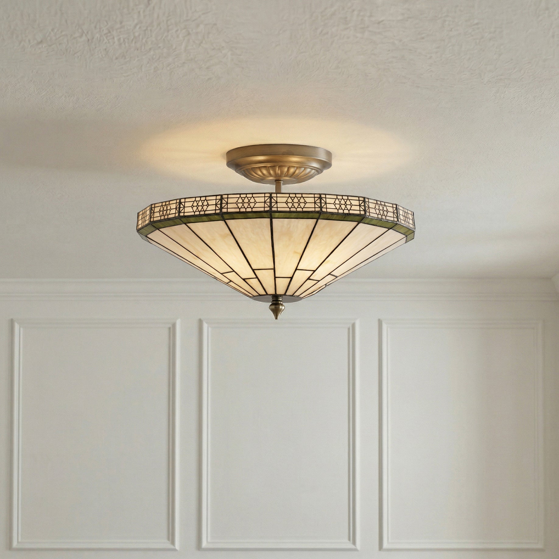 Ceiling light fixture with decorative glass shade on a white paneled wall.