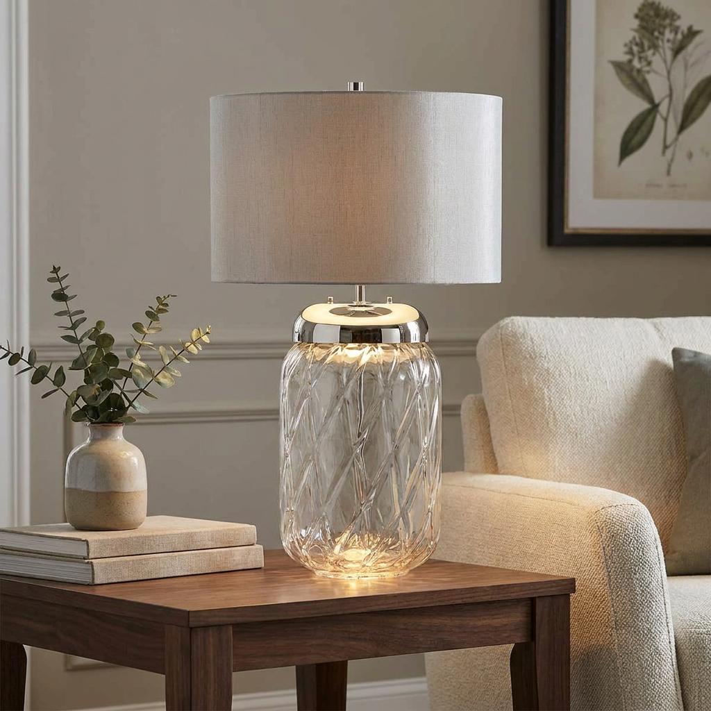 Sola 2 light table lamp with a textured glass base and titanium shade on a wooden side table by an armchair.