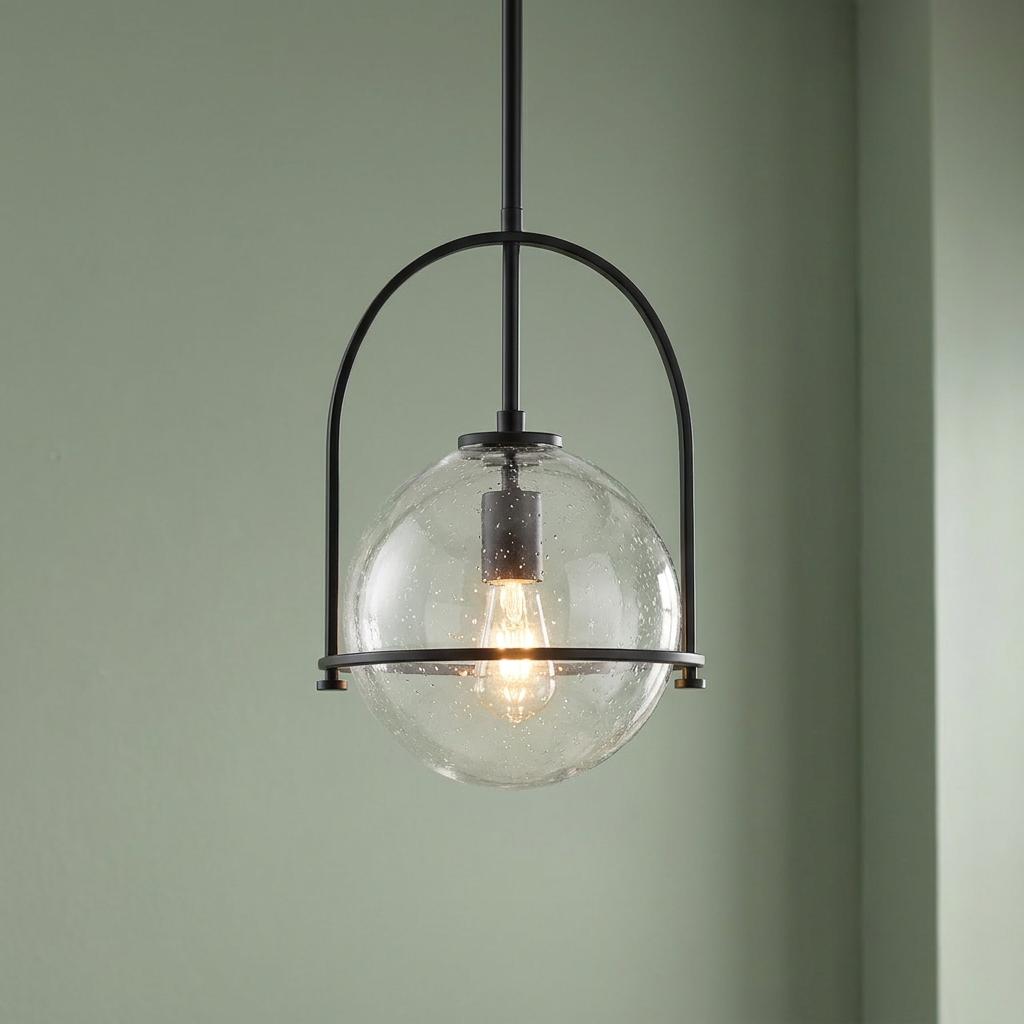 Somerset black pendant light with a clear seeded glass globe and an illuminated bulb against a green wall.