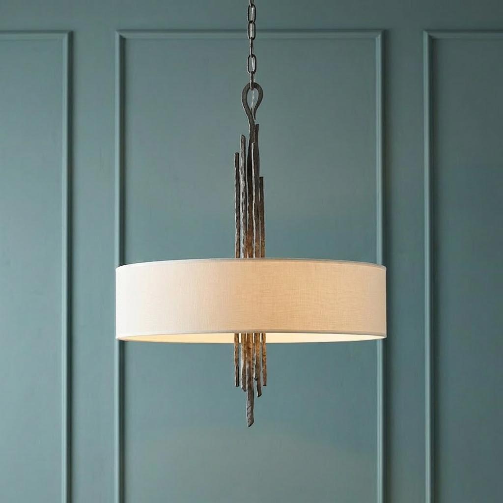 A bronze pendant light with a white drum shade and textured vertical spikes against a teal paneled wall.