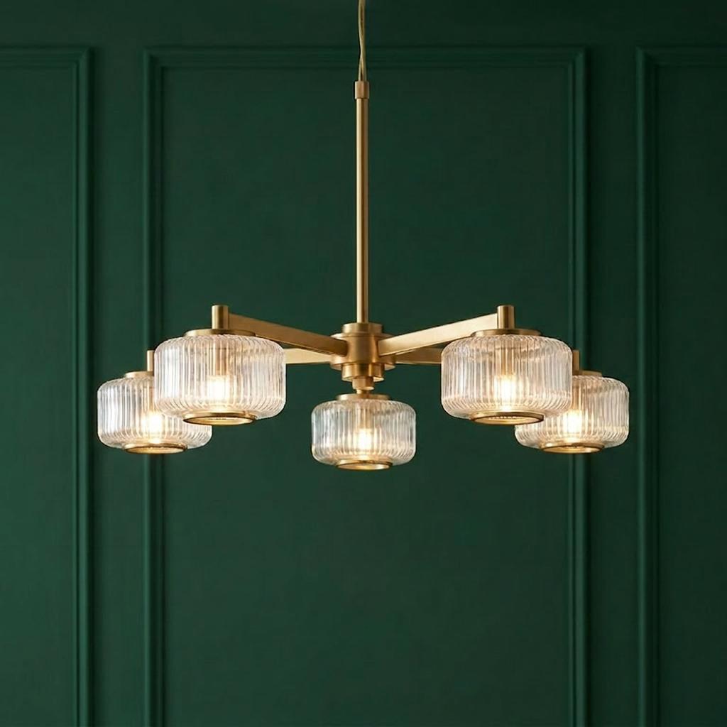 A five-light brass pendant chandelier with ribbed glass shades set against a dark green paneled wall.