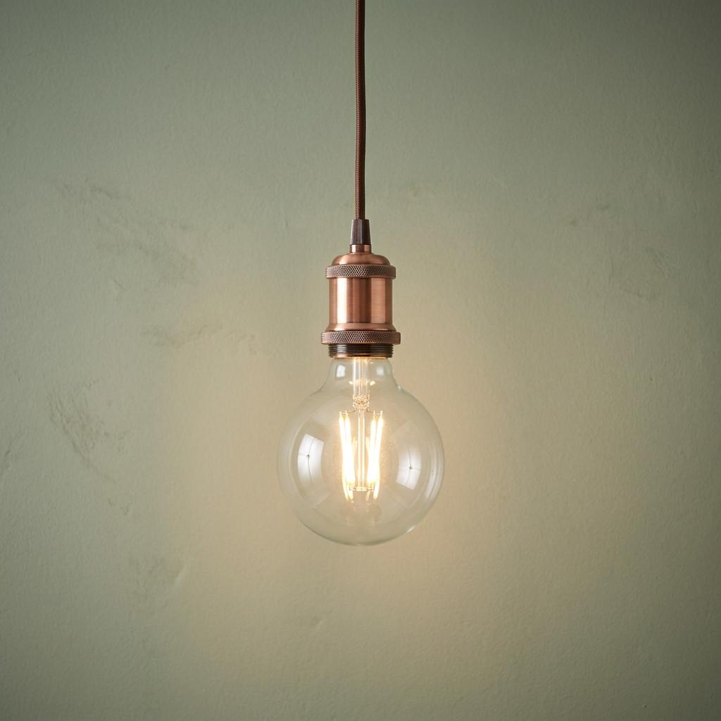 Illuminated clear globe bulb with copper socket and fabric cable against a textured green background.