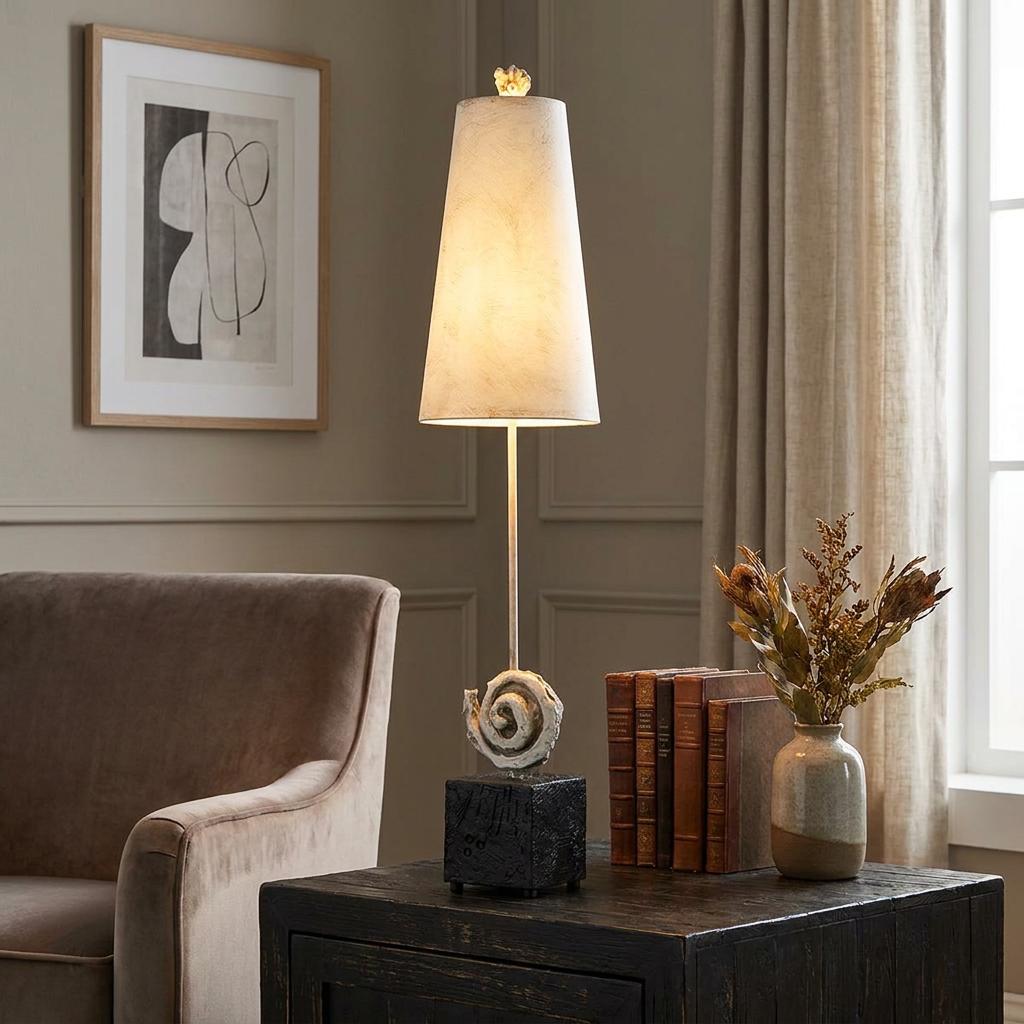 Tall table lamp with a tapered bone-white shade and a spiral base, standing on a dark side table by an armchair.