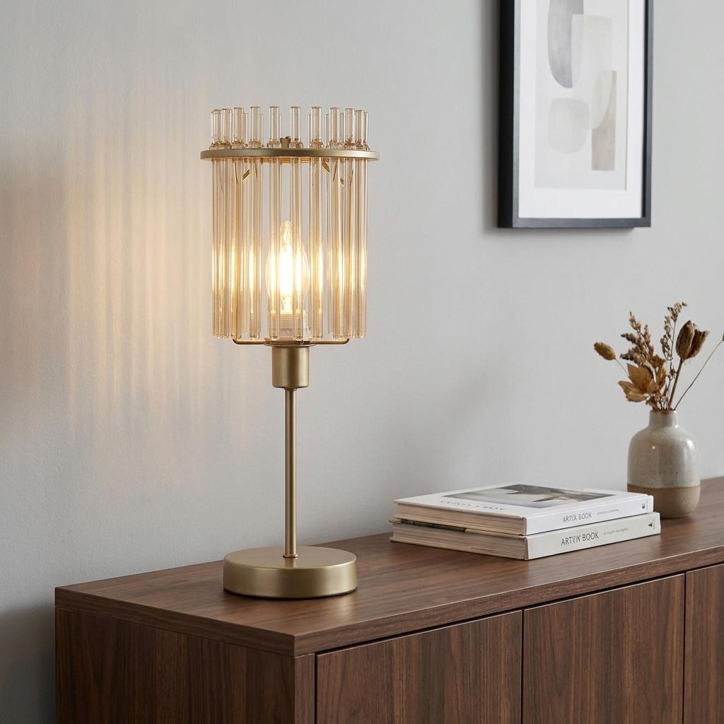 Swizzle gold and champagne table lamp with a glass rod shade illuminated on a wooden sideboard.