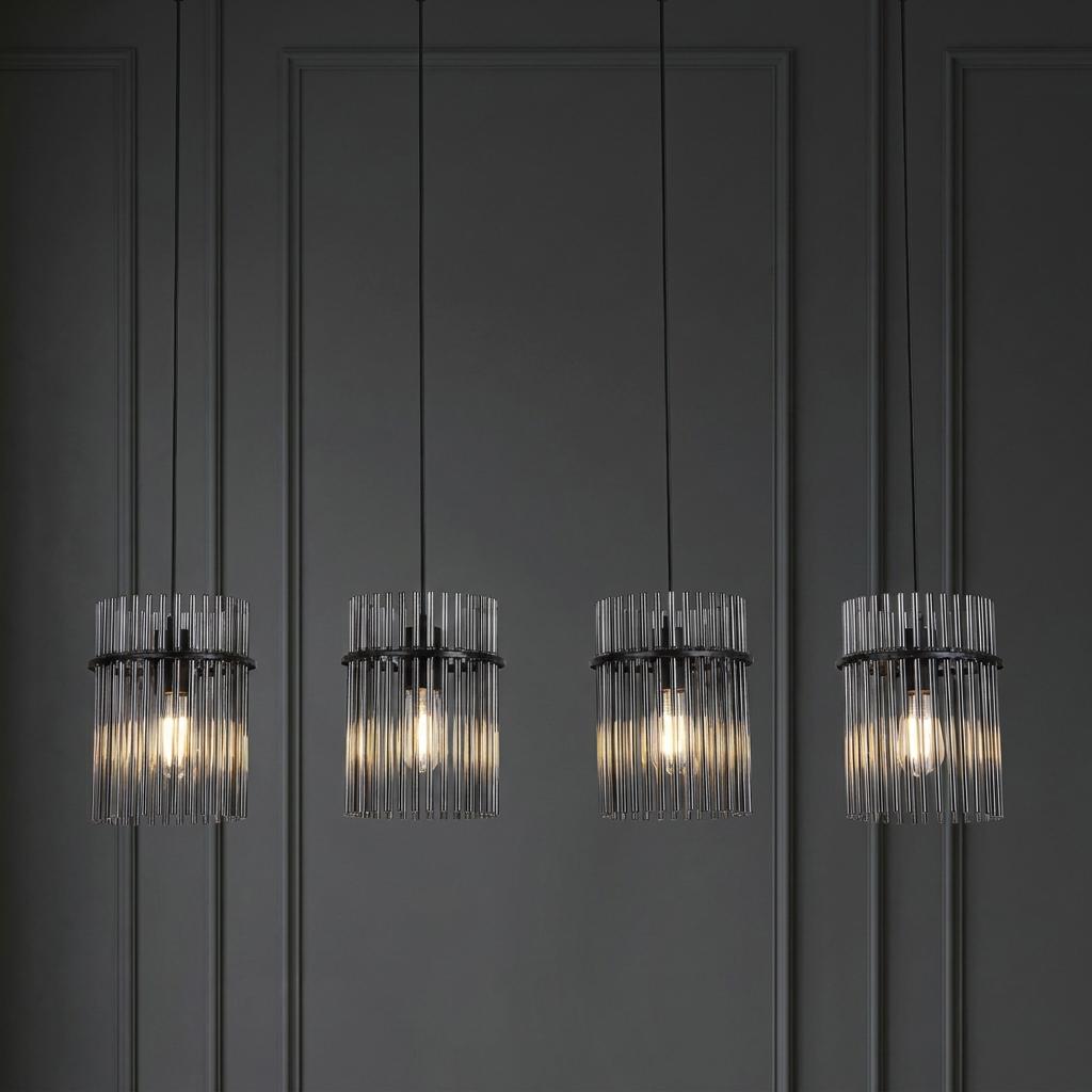 Four Swizzle matt black pendant lights with smoked glass rods against a dark grey paneled wall.