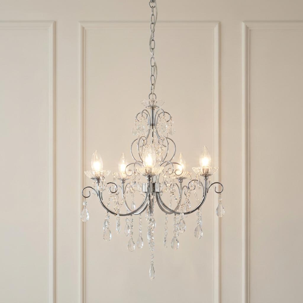 Tabitha 5-light chrome and crystal chandelier with glowing bulbs and hanging droplets against a cream paneled wall.