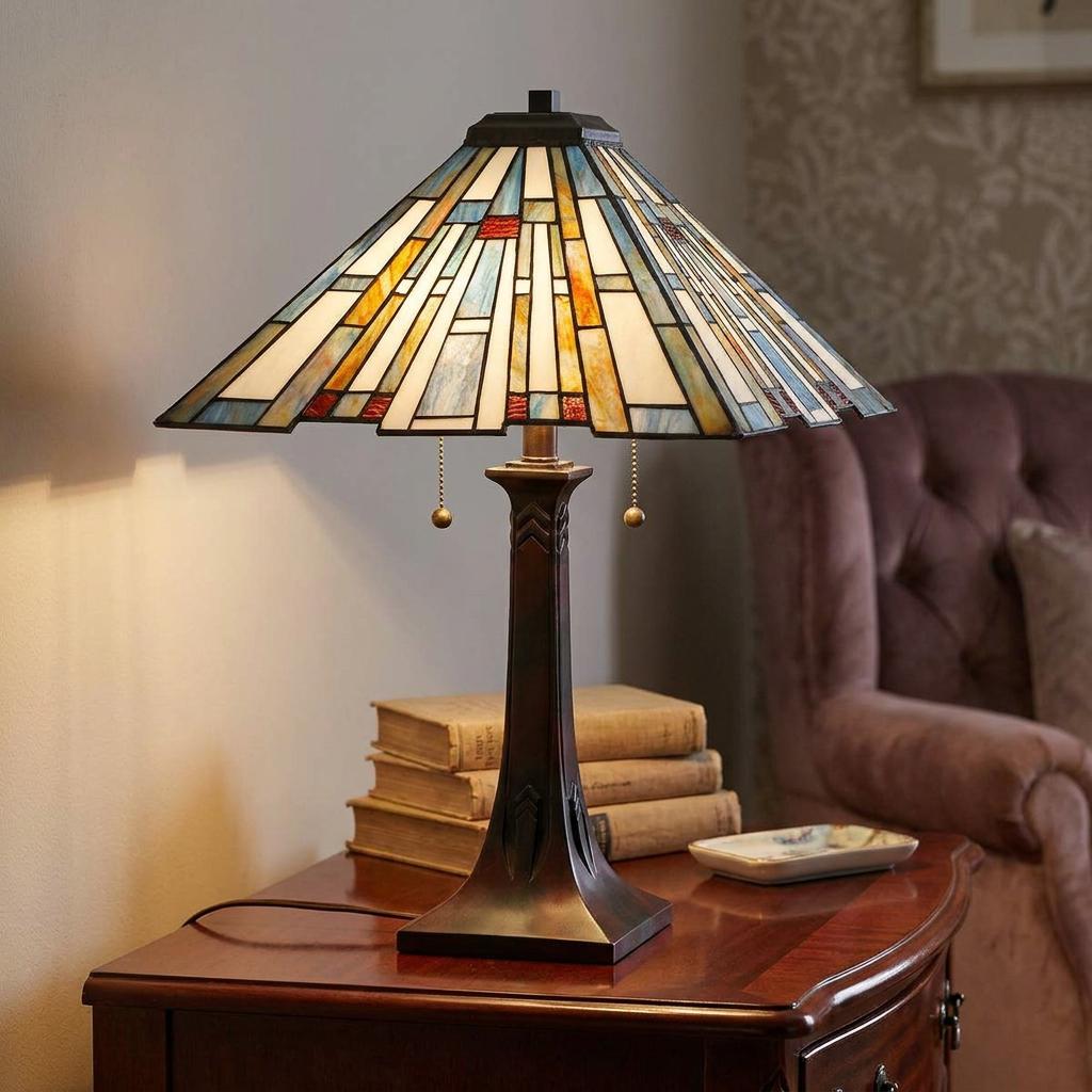 Tiffany-style table lamp with a geometric stained glass shade and bronze base on a wooden side table.