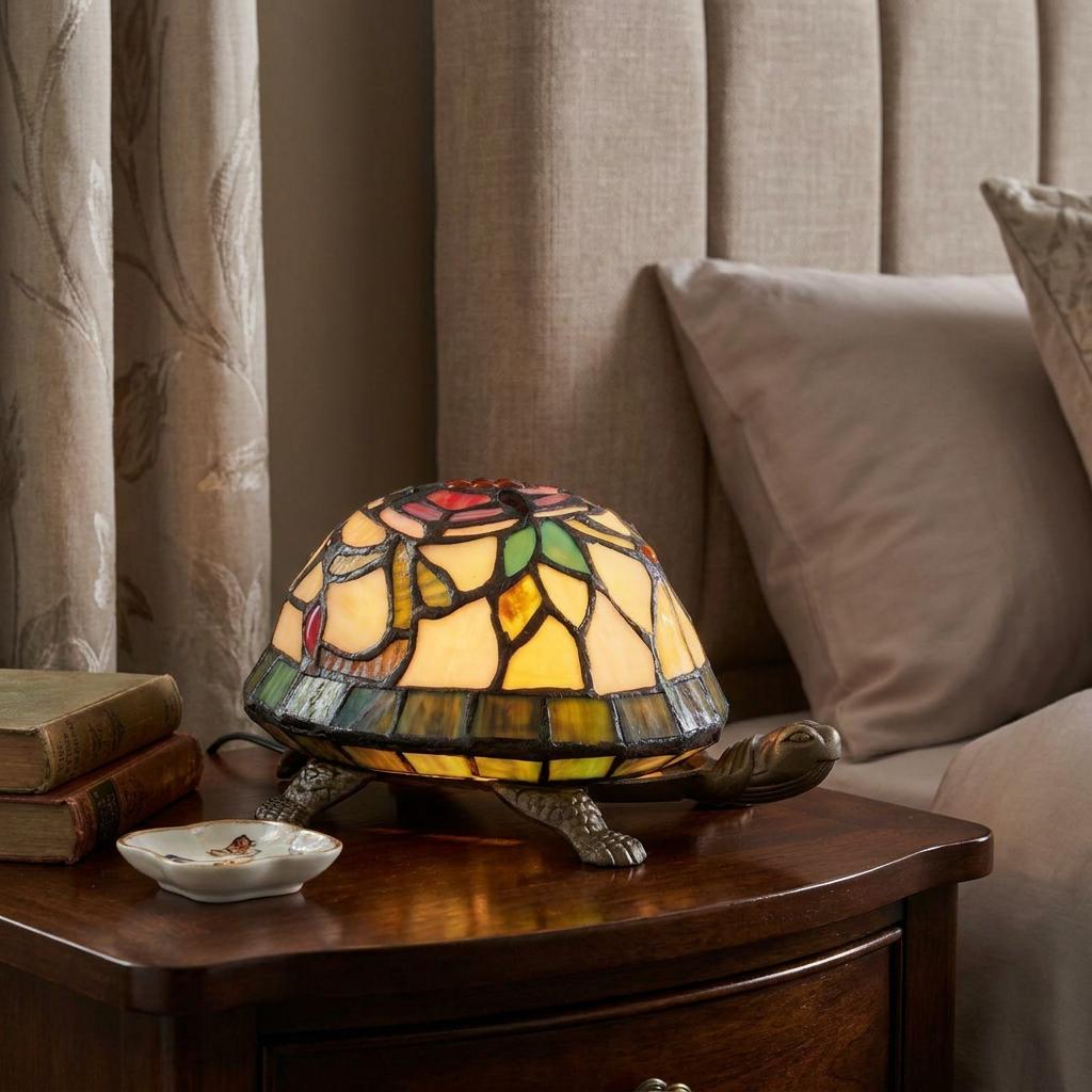 Lit Tiffany-style tortoise lamp with a colorful stained glass shell on a wooden bedside table.