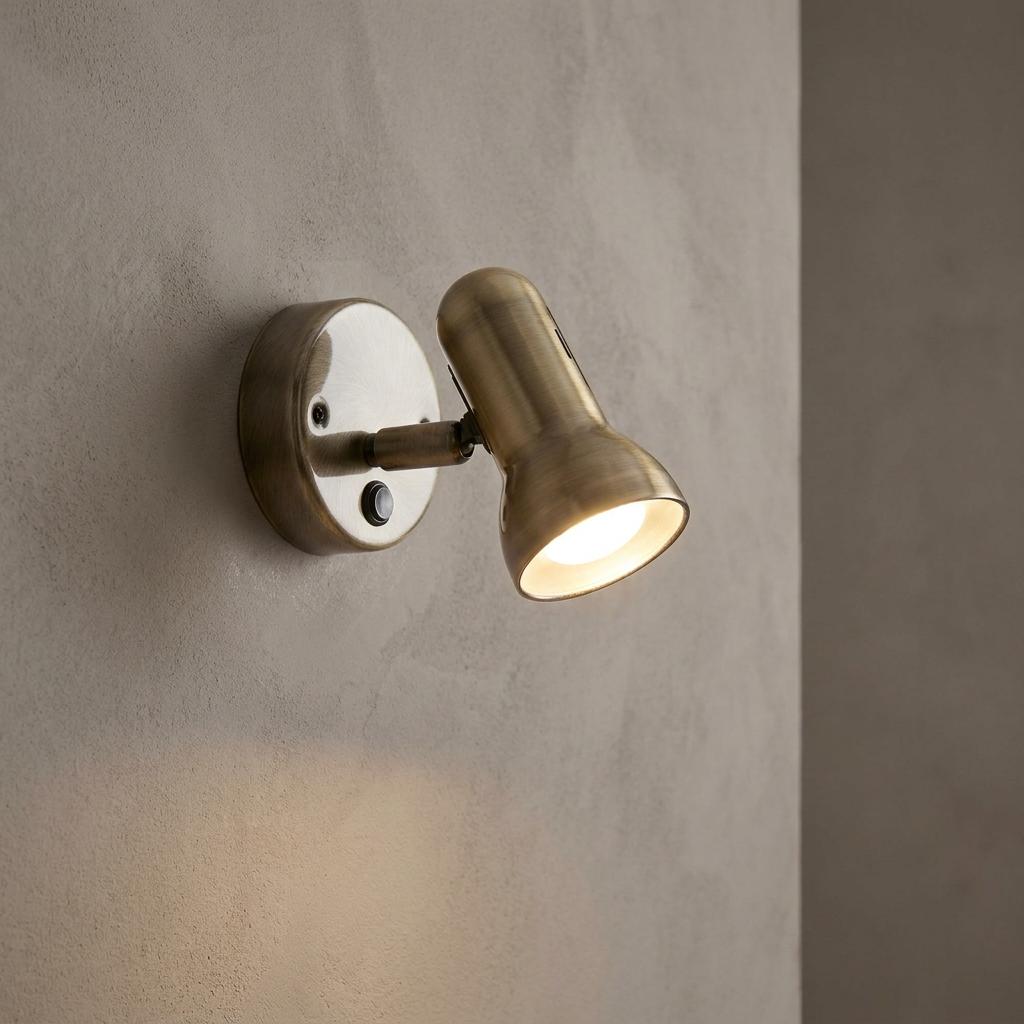 Antique brass single spotlight with an adjustable head and switch, mounted on a neutral textured wall.