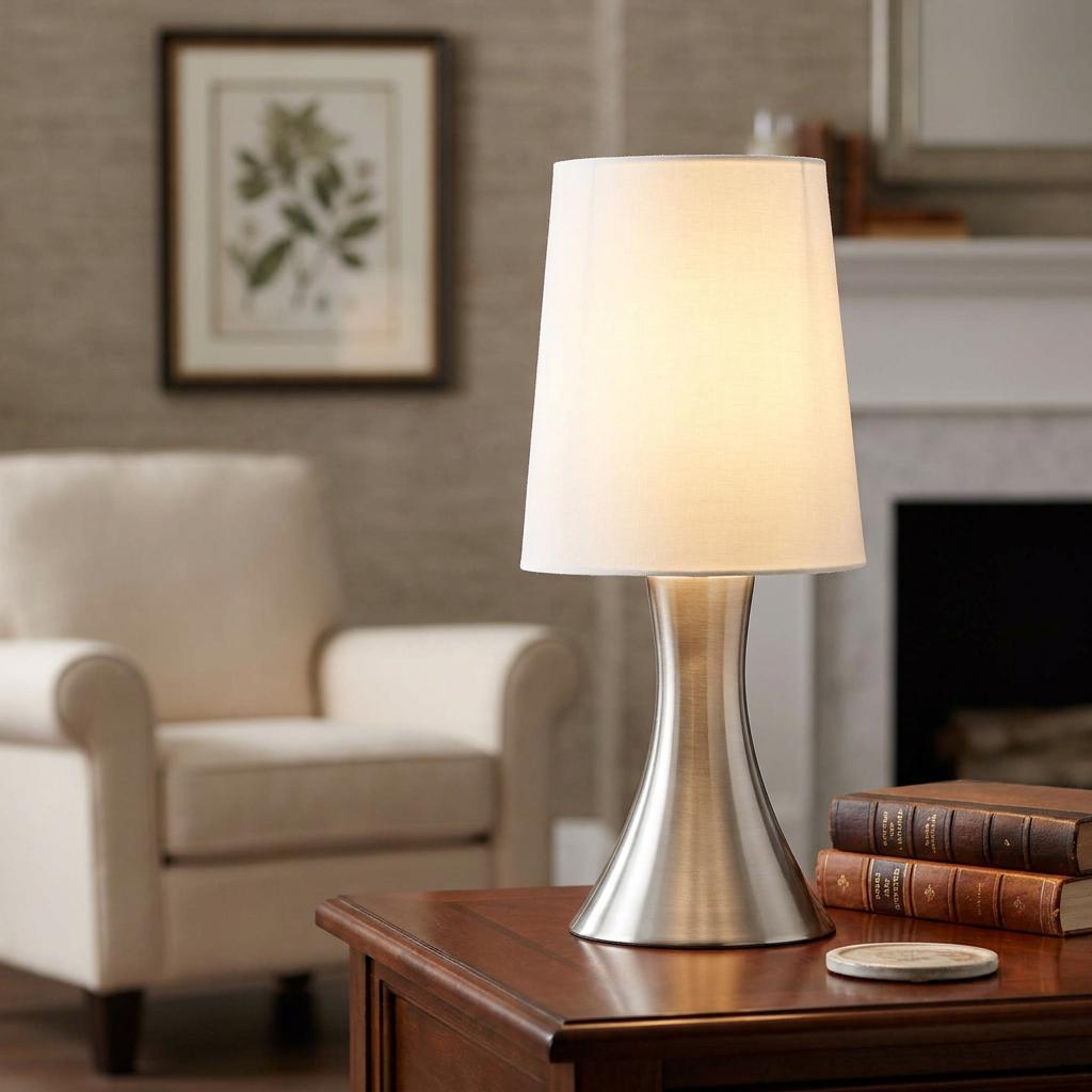 Satin silver touch table lamp with a white tapered shade on a wooden side table in a living room.