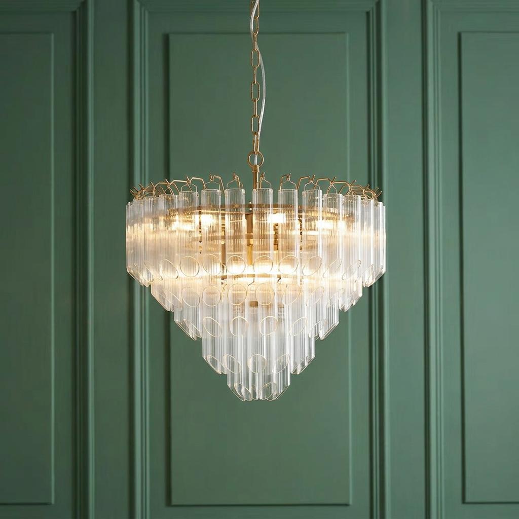 A tiered brass and ribbed glass chandelier hangs illuminated against a sage green paneled wall.