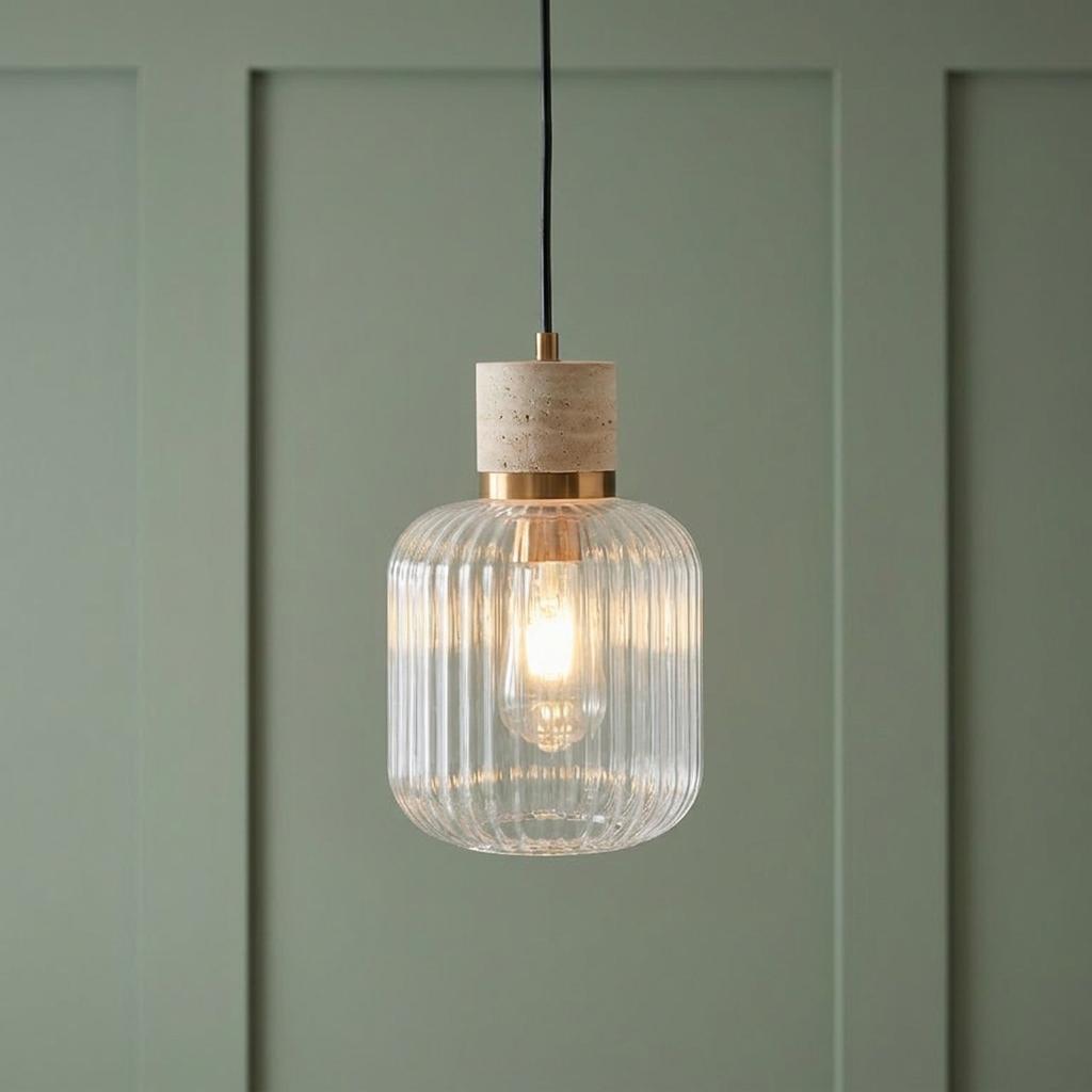 Lit ribbed glass pendant light with brass and travertine stone accents against a sage green paneled wall.