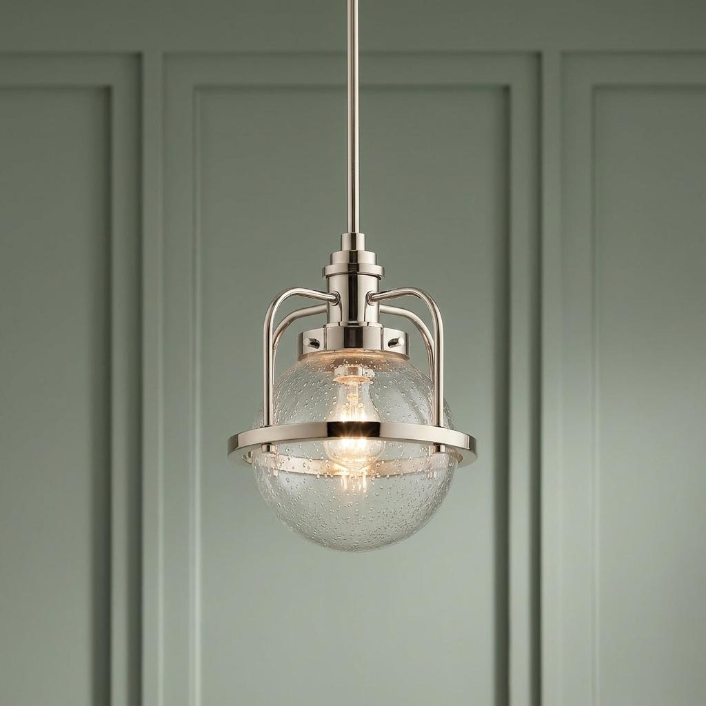 Polished nickel pendant light with a seeded glass globe hanging against a sage green paneled wall.