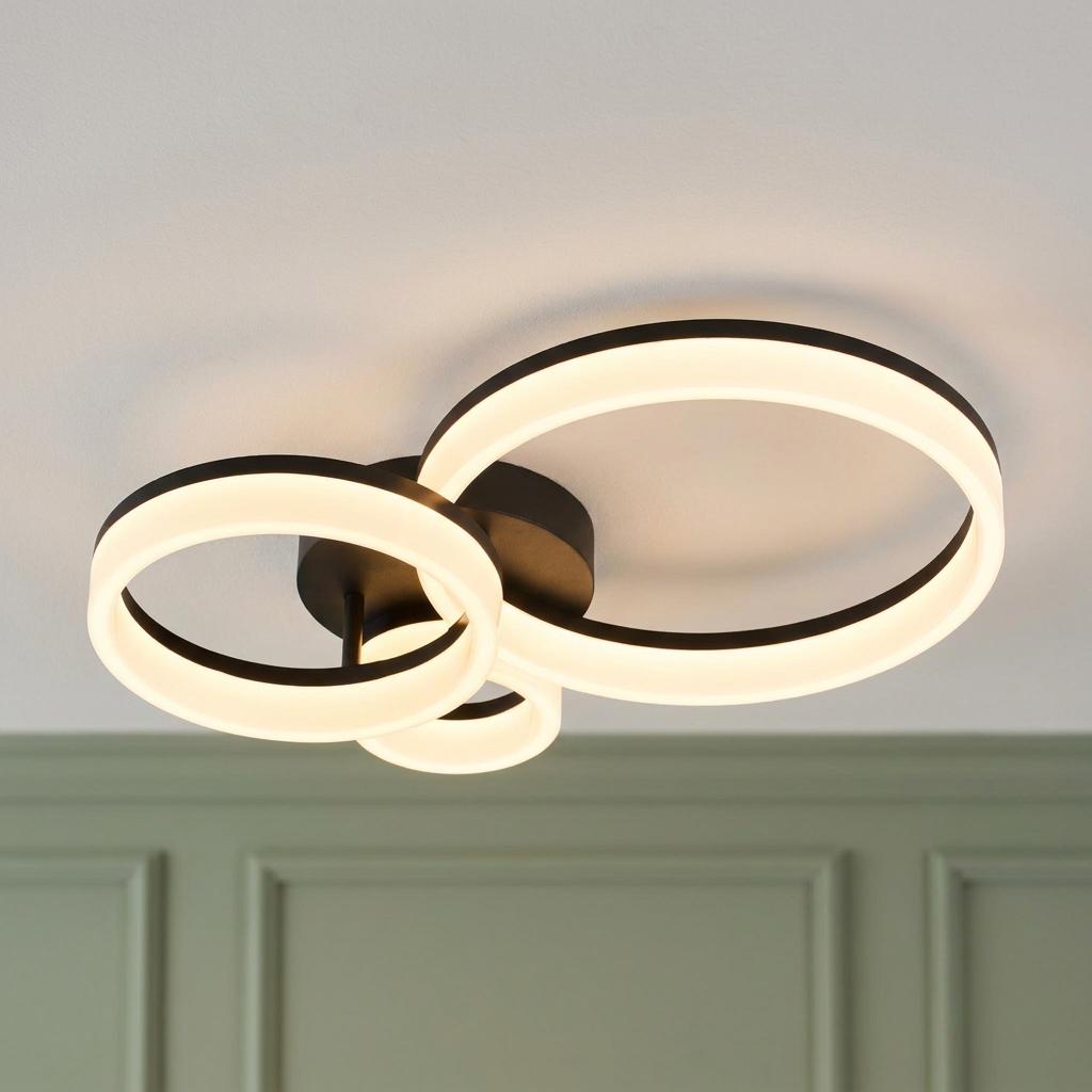 Modern matte black flush ceiling light featuring three interlocking glowing LED rings against a light ceiling.