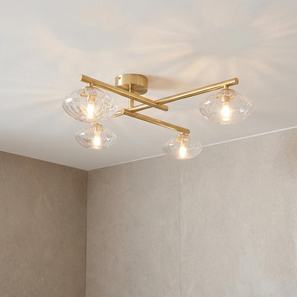 Modern brass semi-flush ceiling light with four ribbed glass shades mounted on crossed arms in a bathroom setting.
