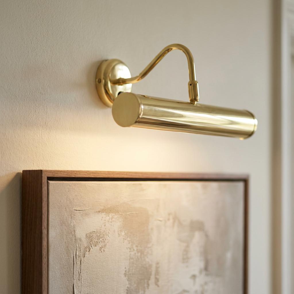A polished brass LED picture light mounted on a wall, illuminating a framed piece of art.
