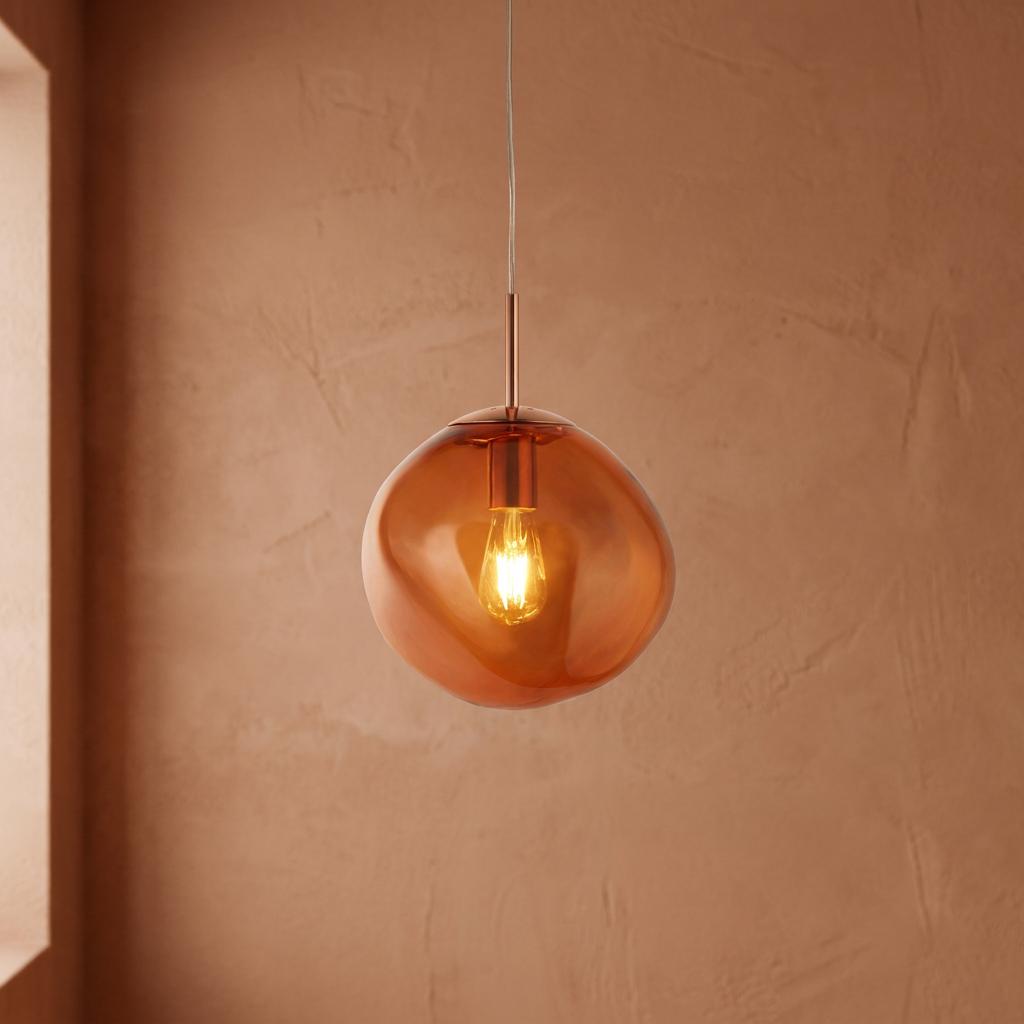 Twisted amber glass pendant light with a copper fitting, hanging against a textured peach wall.