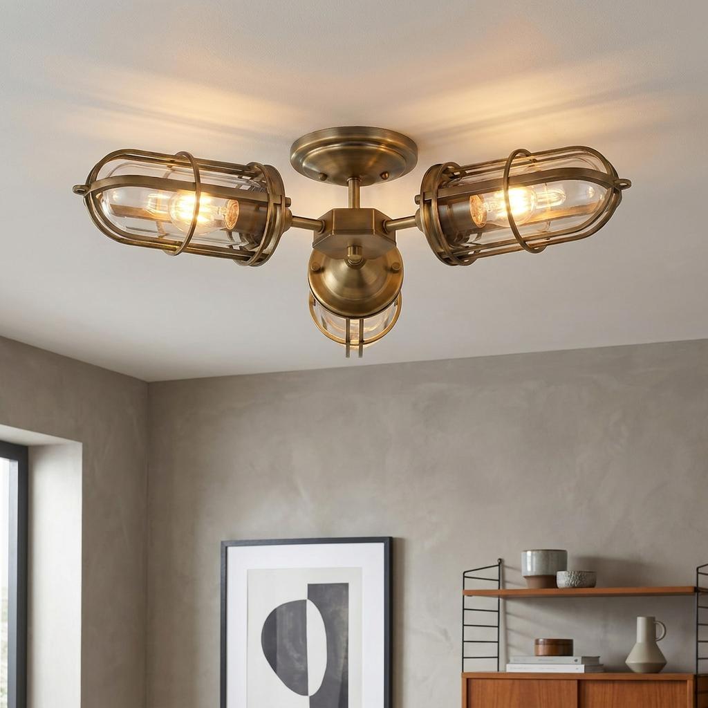 Three-light industrial brass ceiling fixture with caged glass shades illuminated in a modern room.