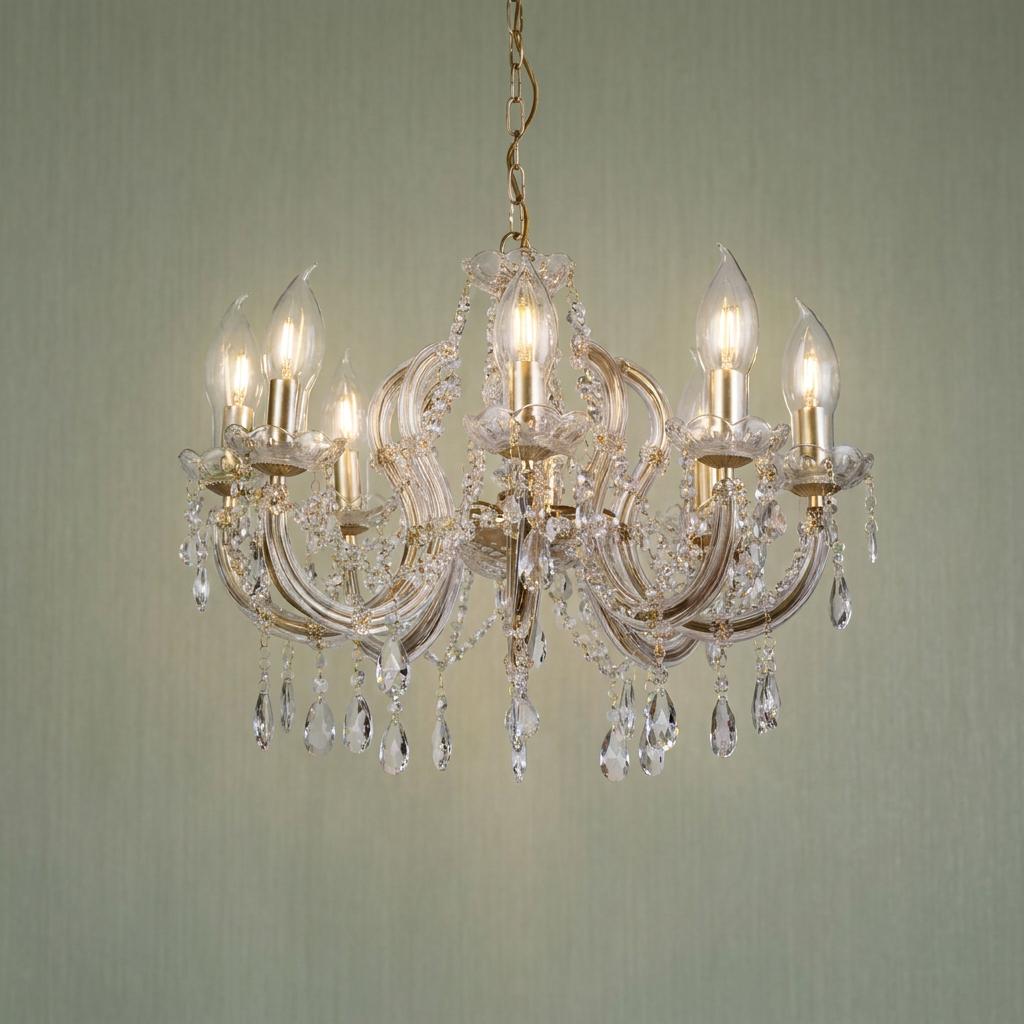 An ornate gold and crystal pendant chandelier with lit candle-style bulbs against a green textured wall.