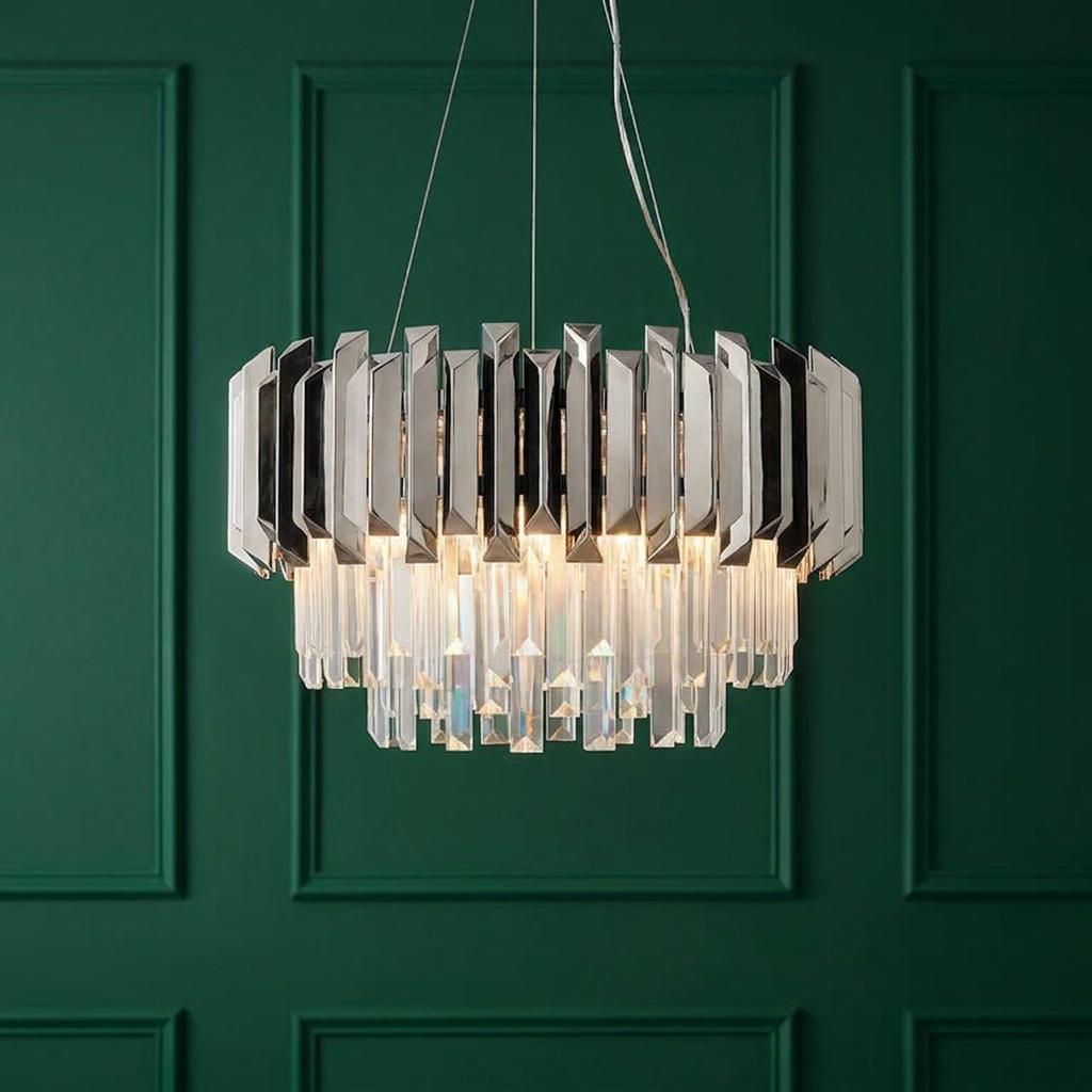 Polished stainless steel and crystal tiered pendant light glowing against a dark green paneled wall.