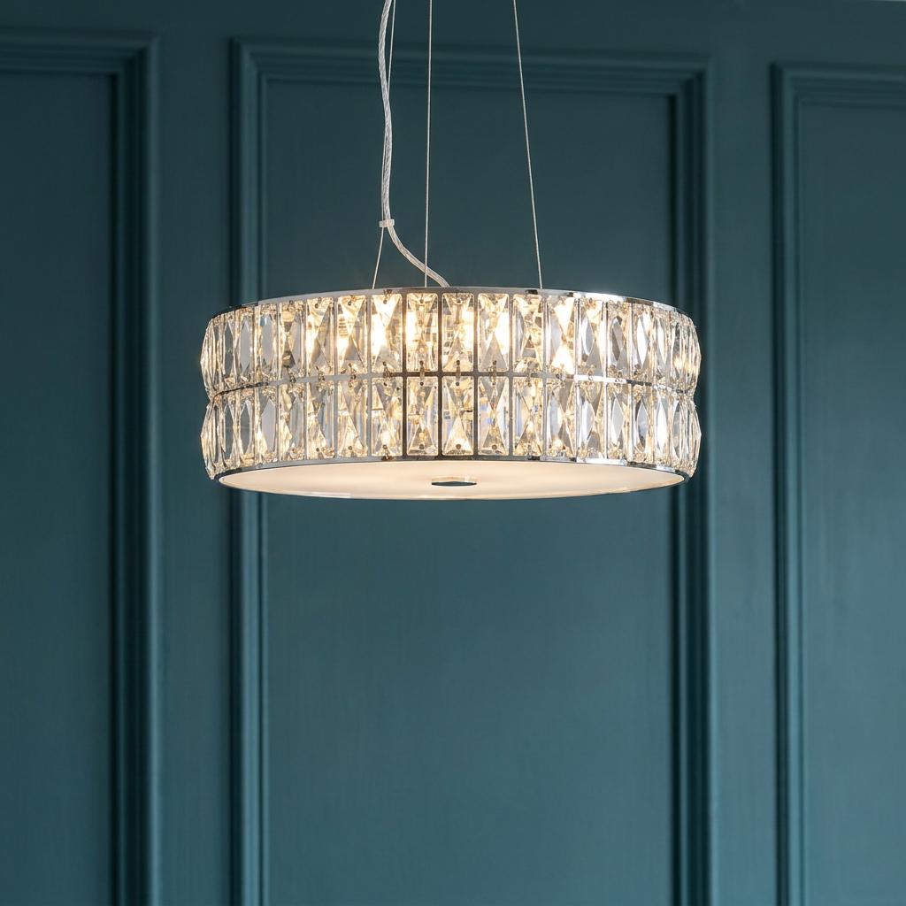 A drum-shaped chrome and crystal pendant light illuminated against a dark teal paneled wall.