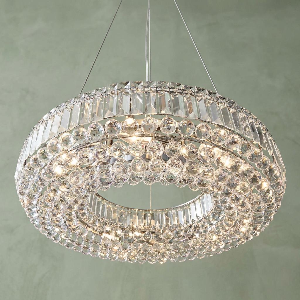 Circular chrome pendant light with tiered crystal spheres and rectangular prisms hanging against a green wall.