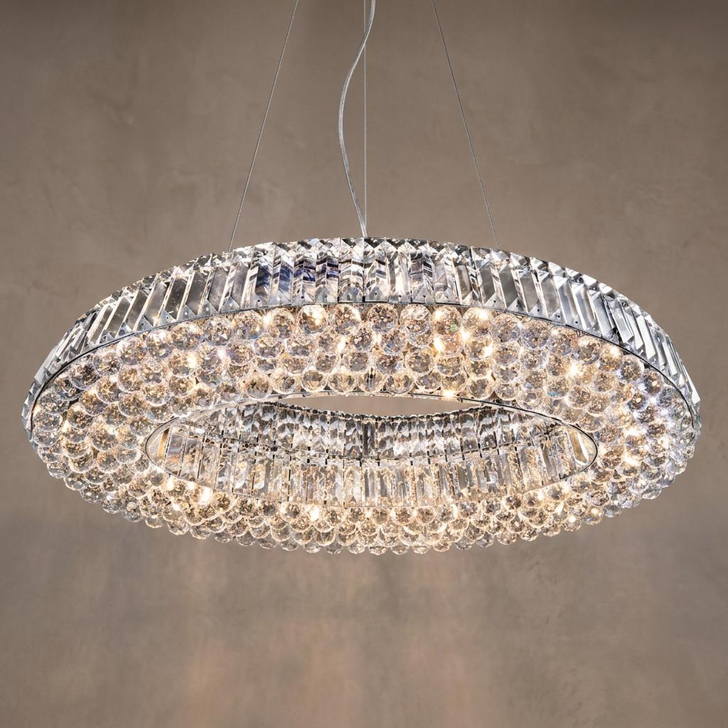 Oval chrome chandelier featuring clear crystal spheres and faceted glass baguettes, illuminated against a textured wall.