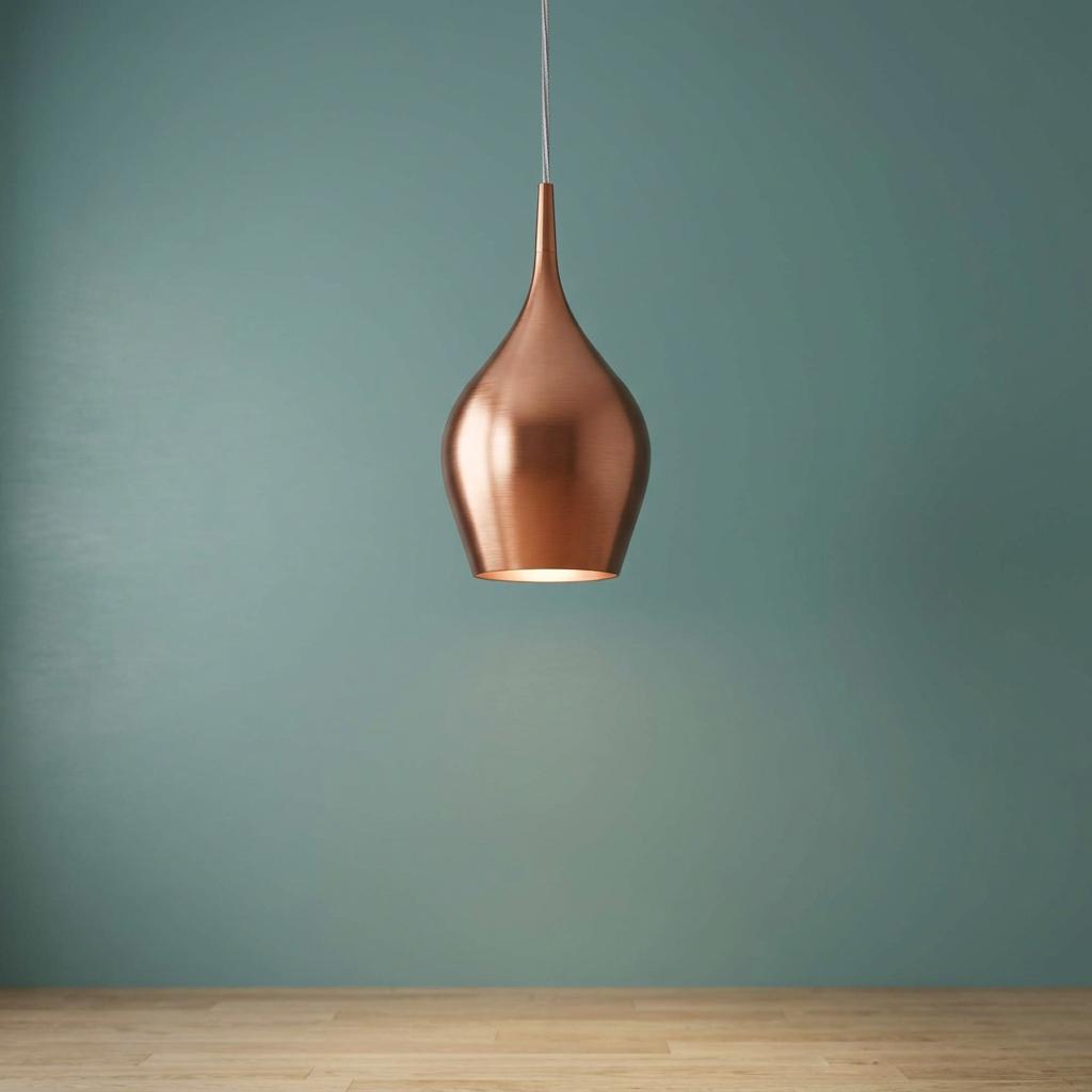 Teardrop-shaped copper pendant lamp hanging in front of a minimalist teal wall above a wooden floor.