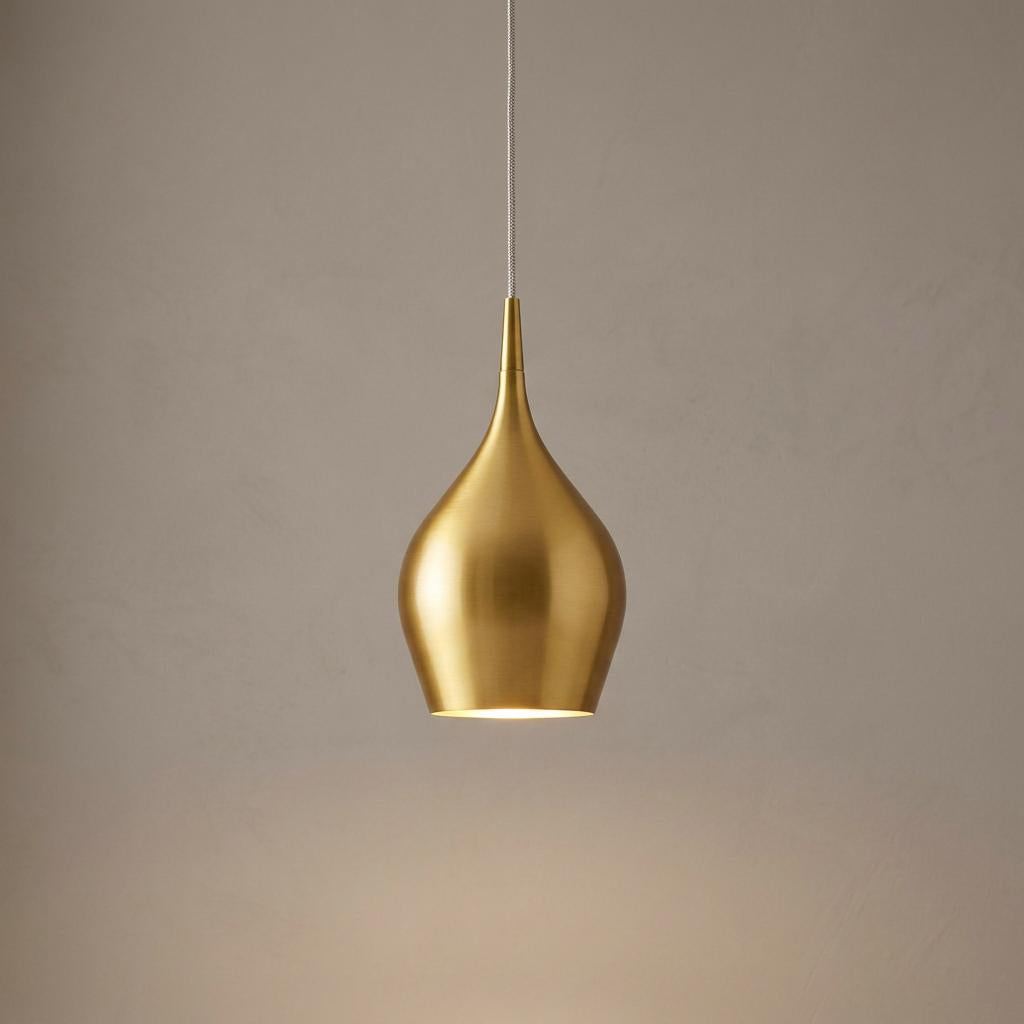A modern teardrop-shaped gold metal pendant light illuminated against a neutral wall.