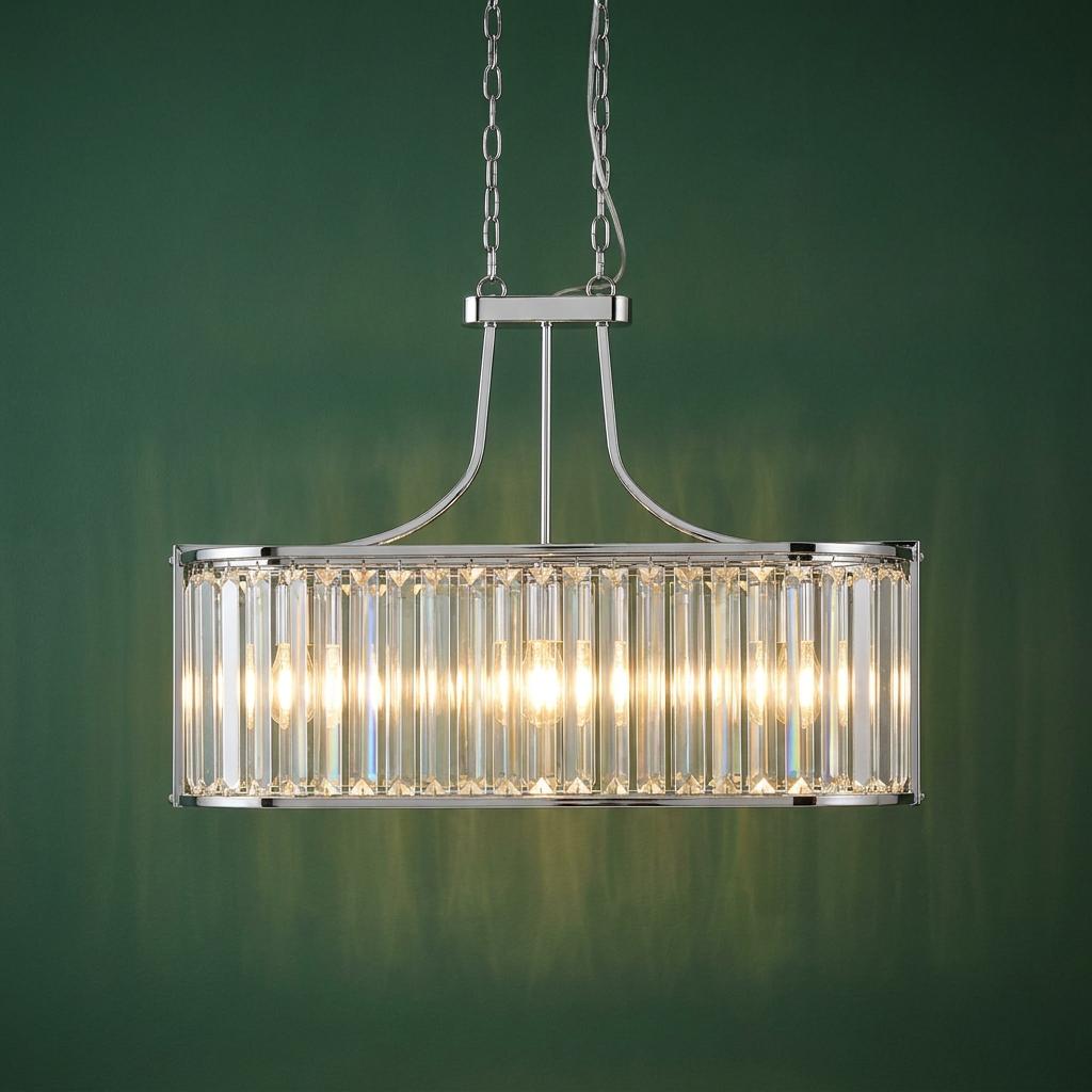 Modern oval chrome pendant light with crystal glass prisms illuminated against a dark green wall.