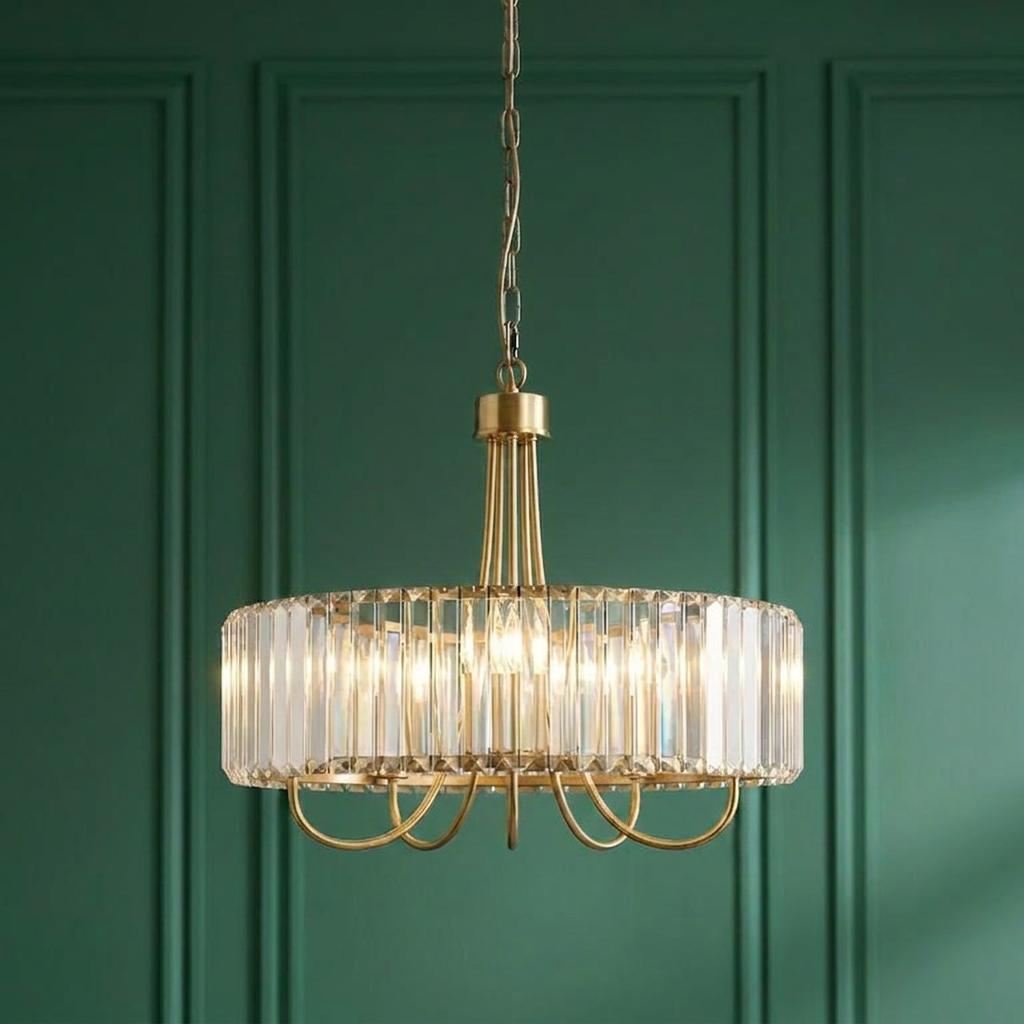 Round brass pendant light with clear cut glass crystals hanging against a dark green paneled wall.