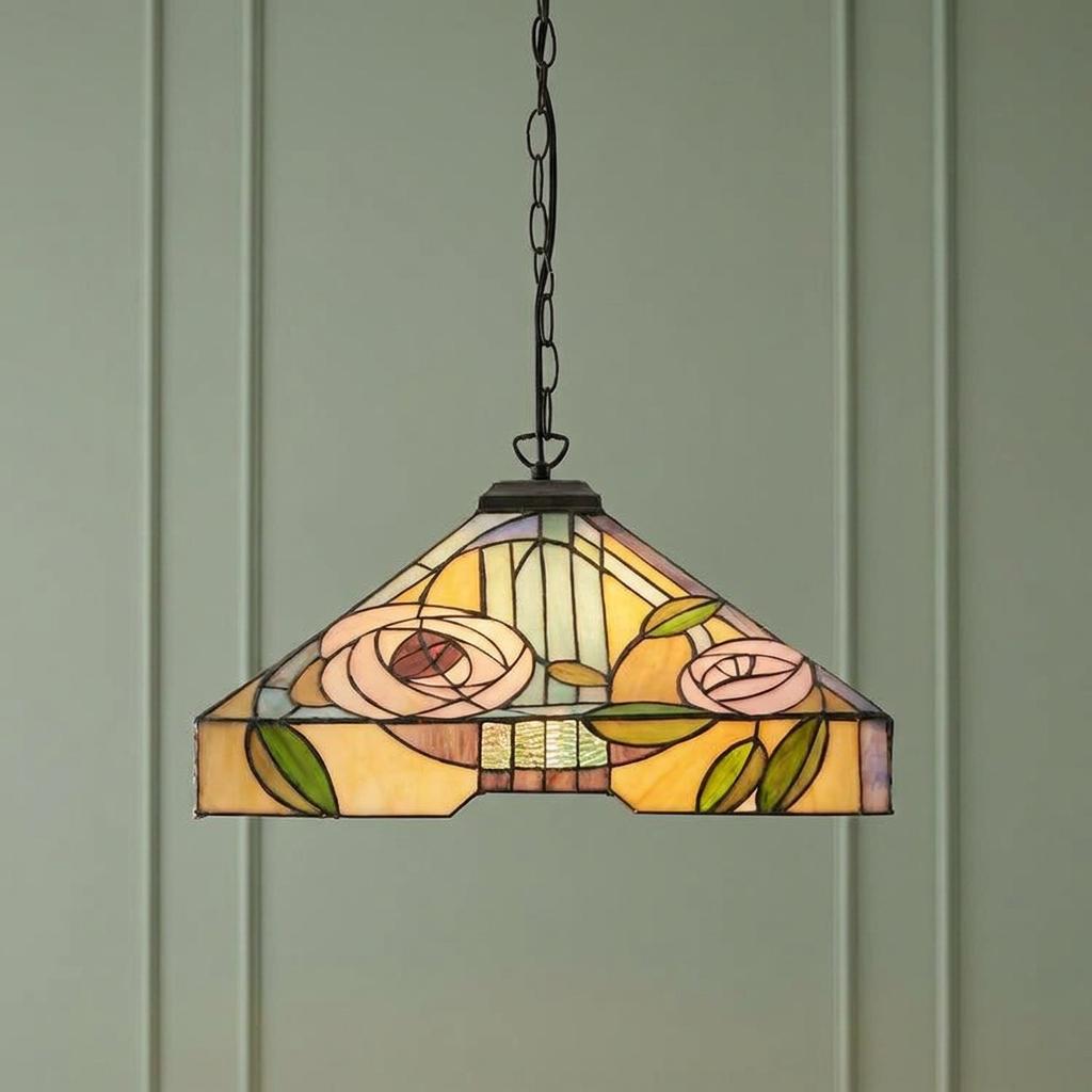 Stained glass Tiffany pendant light with a pink rose design hanging against a pale green paneled wall.