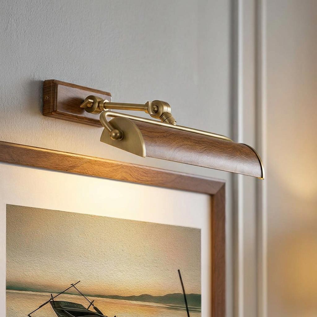 Medium oak picture light with brass hardware illuminating a framed landscape painting on a wall.