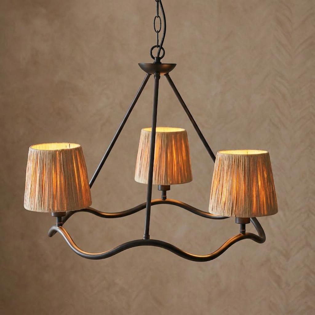 A three-light ceiling pendant with a wavy black metal frame and textured raffia shades against a neutral wall.