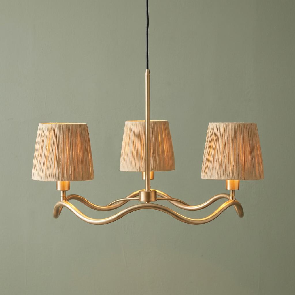 Wriggle Brass 3 Light Pendant with a wavy frame and textured beige shades against a sage green wall.